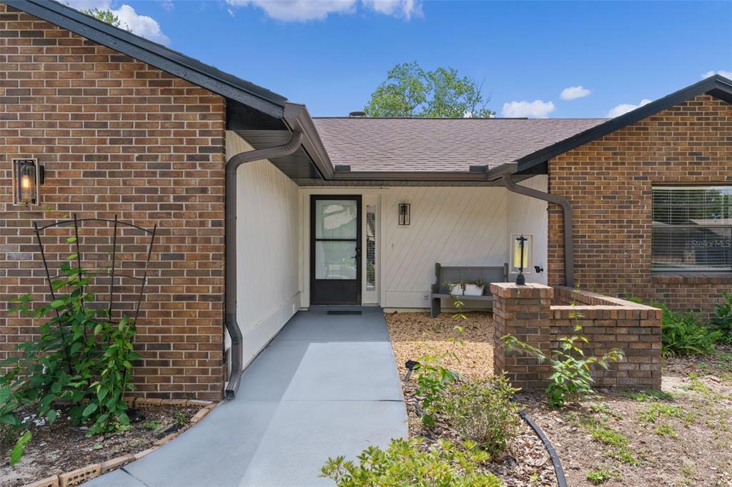 A brick house exterior features a covered entryway with a concrete walkway and bench — 1401 14TH STREET, CLERMONT, FL