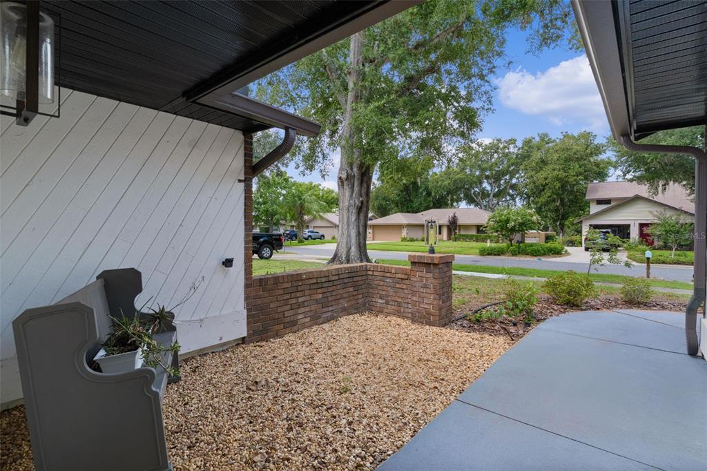 A covered front porch features a brick wall, gravel ground, and a gray bench — 1401 14TH STREET, CLERMONT, FL