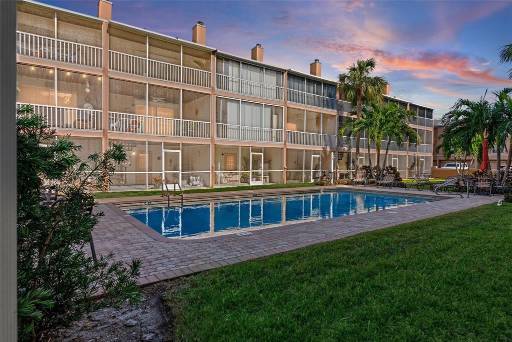 A multi-story apartment building with screened balconies overlooks a rectangular swimming pool and lawn — 637 PINELLAS BAYWAY S UNIT 207, TIERRA VERDE, FL