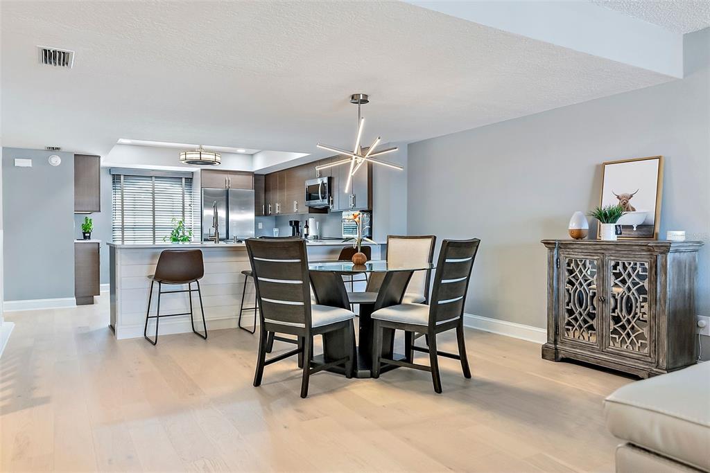 A dining area with a glass table and modern chandelier sits beside a kitchen island — 637 PINELLAS BAYWAY S UNIT 207, TIERRA VERDE, FL