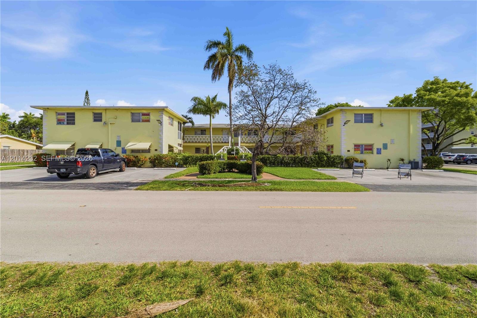 A two-story yellow apartment building features a central courtyard, palm trees, and a parking lot — 1501 Arthur St # 6, Hollywood FL 33020, HOLLYWOOD, FL
