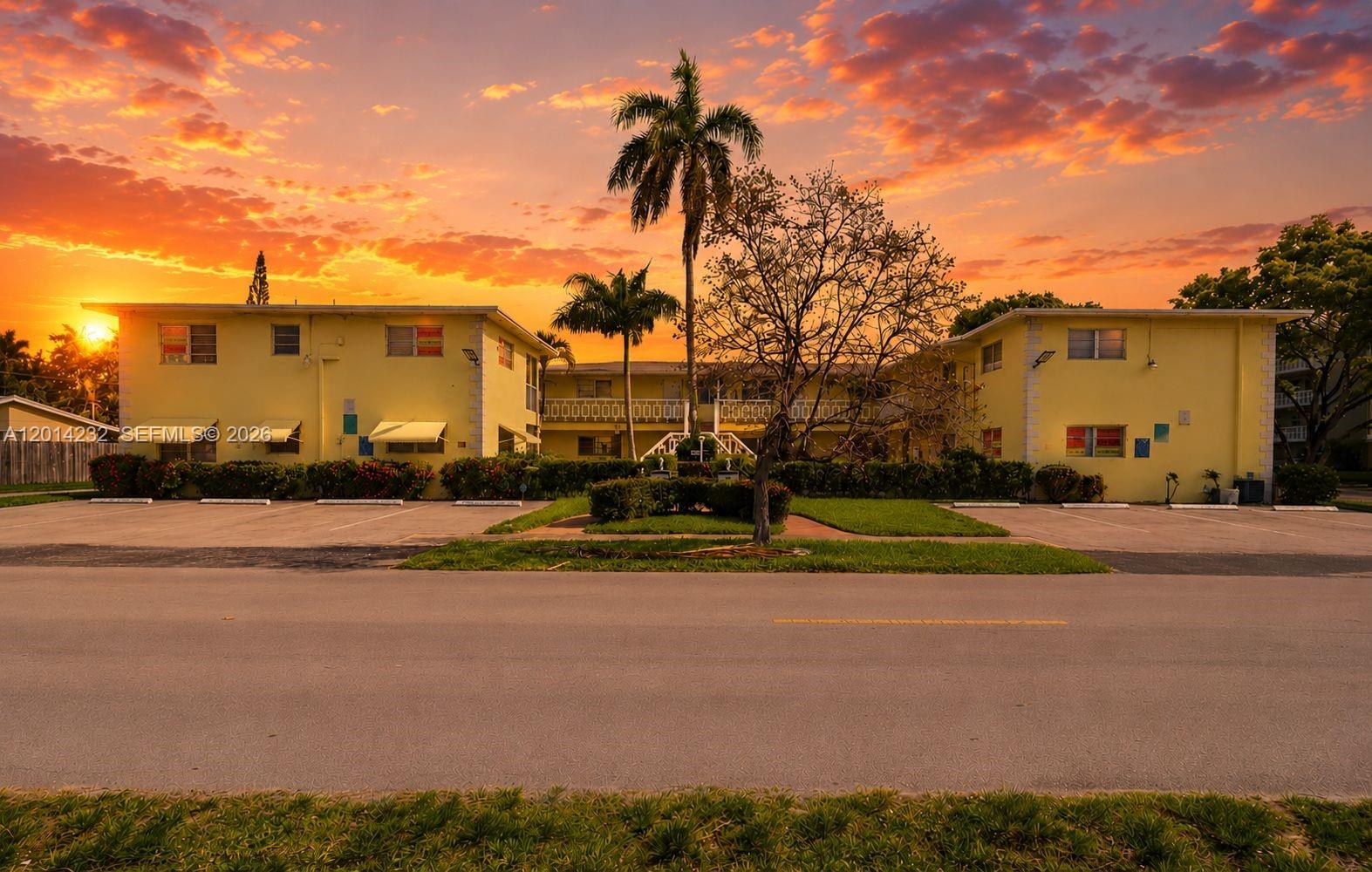 A two-story yellow apartment building stands behind a parking lot under a sunset sky — 1501 Arthur St # 6, Hollywood FL 33020, HOLLYWOOD, FL