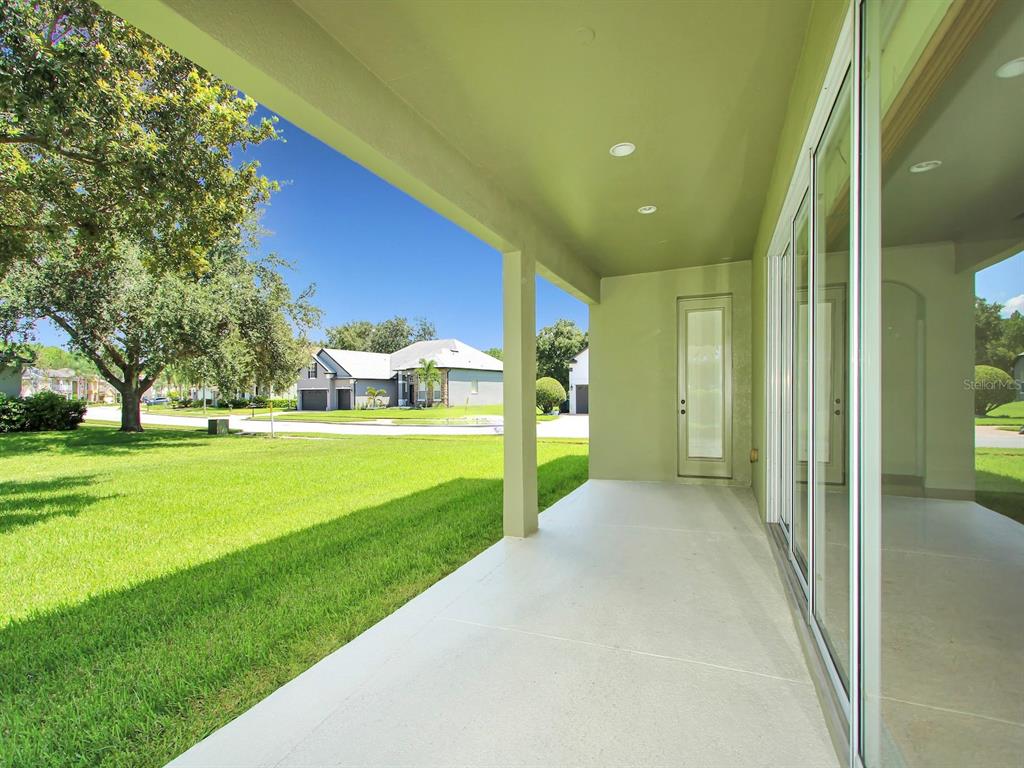 A covered concrete patio overlooks a grassy lawn and neighboring houses on a sunny day — 10093 CHARDONNAY DRIVE, ORLANDO, FL