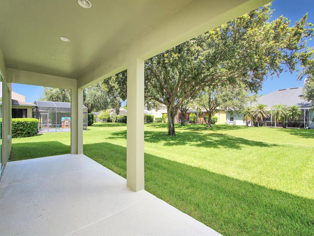 A covered concrete patio overlooks a large grassy backyard with mature trees and neighboring houses — 10093 CHARDONNAY DRIVE, ORLANDO, FL
