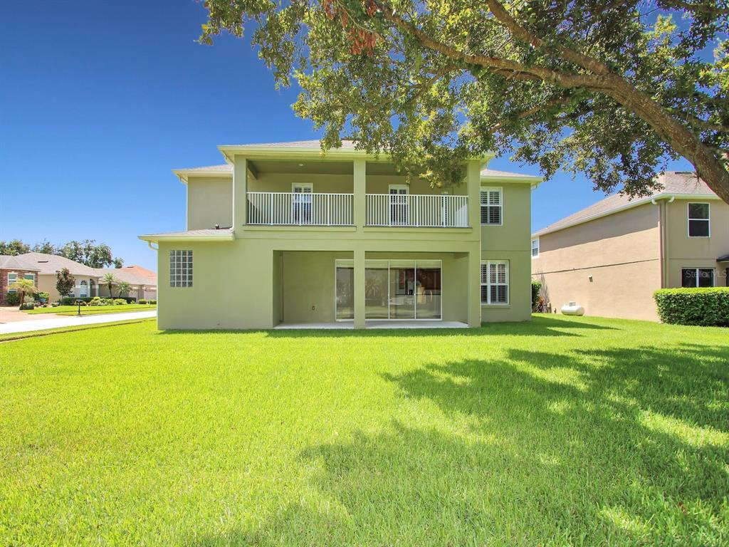 The rear exterior of a two-story house features a covered patio and an upper balcony — 10093 CHARDONNAY DRIVE, ORLANDO, FL
