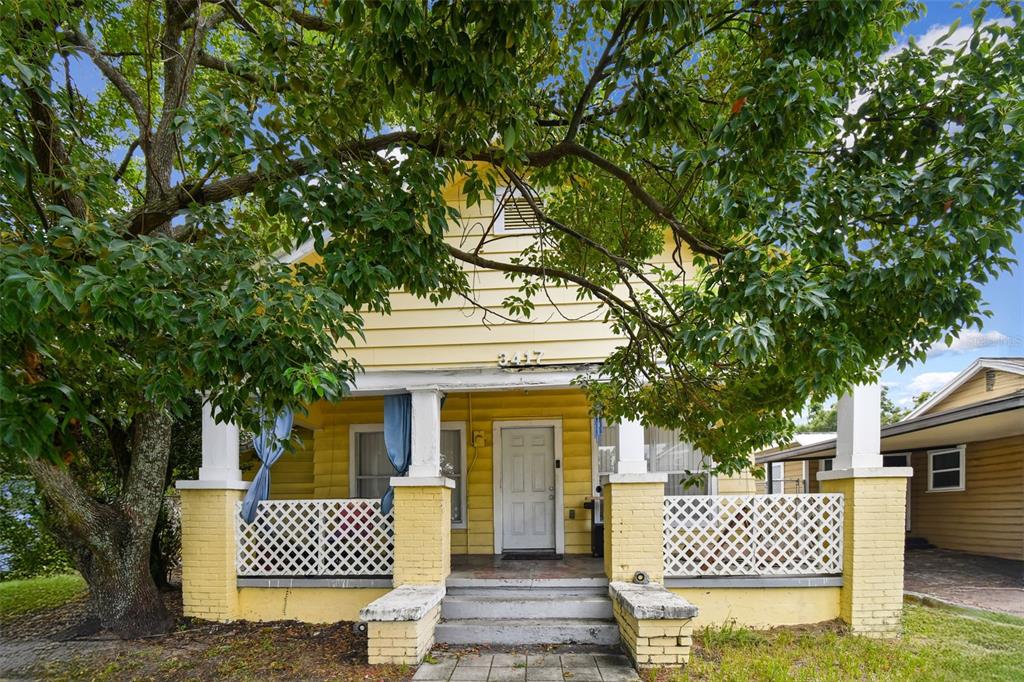 A yellow two-story house features a front porch with white lattice railings and brick pillars — 3417 E LAKE AVENUE, TAMPA, FL