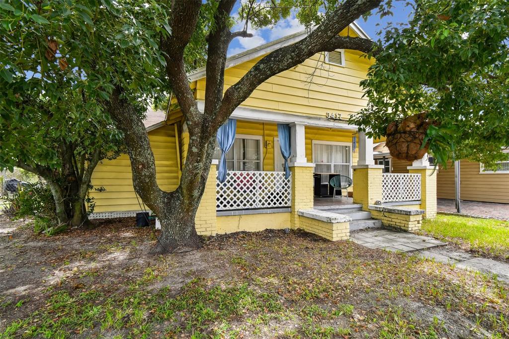 A yellow, single-story house features a front porch with white lattice railings and blue curtains — 3417 E LAKE AVENUE, TAMPA, FL