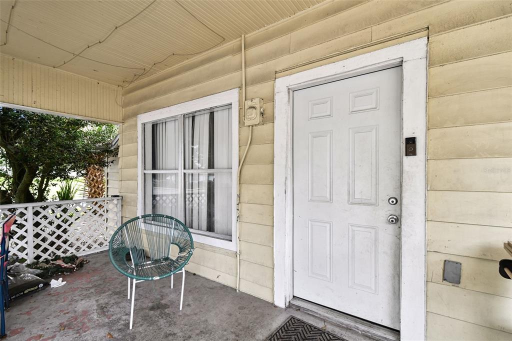 A covered porch features light-colored siding, a white front door, and a green patio chair — 3417 E LAKE AVENUE, TAMPA, FL