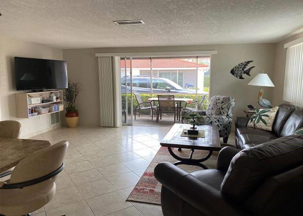 A living room features tile flooring, a television, a leather sofa, and a sliding glass door — 6154 MIDNIGHT PASS ROAD UNIT C06, SARASOTA, FL