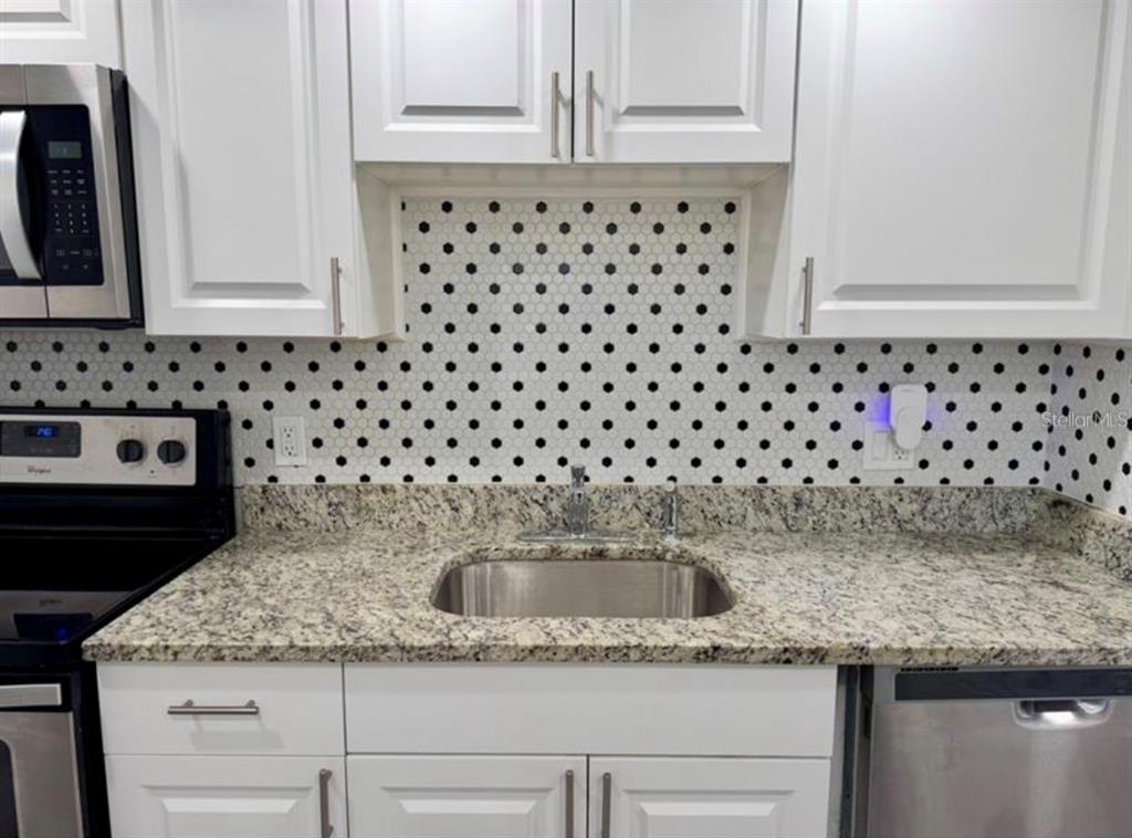 A kitchen features white cabinets, granite countertops, a stainless steel sink, and a polka-dot backsplash — 6312 NEWTOWN CIRCLE UNIT 12C2, TAMPA, FL