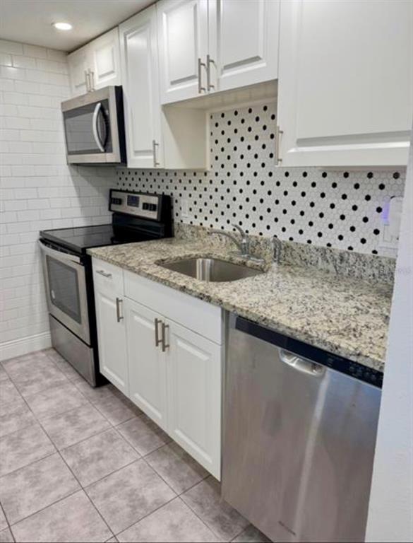 A kitchen features white cabinets, stainless steel appliances, granite countertops, and a polka-dot backsplash — 6312 NEWTOWN CIRCLE UNIT 12C2, TAMPA, FL