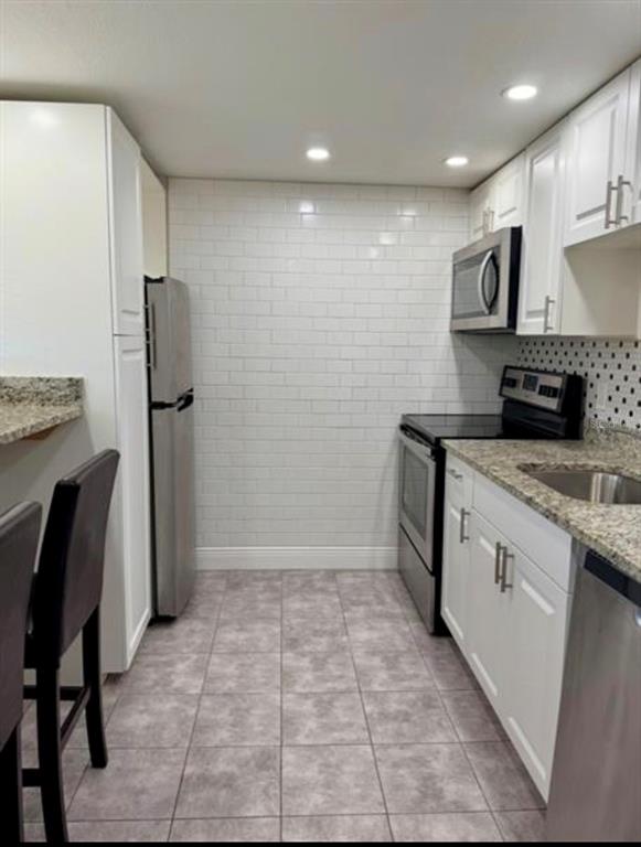 A kitchen features white subway tile walls, white cabinetry, stainless steel appliances, and tile flooring — 6312 NEWTOWN CIRCLE UNIT 12C2, TAMPA, FL