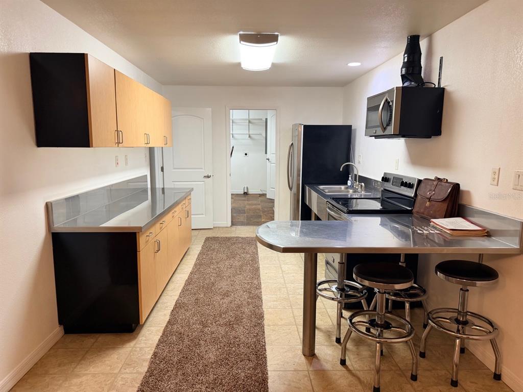A kitchen features light wood cabinets, stainless steel countertops, black appliances, and a breakfast bar — 790 NW 42 TERRACE, CHIEFLAND, FL
