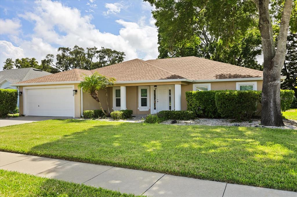A single-story tan house with a two-car garage, a front lawn, and mature landscaping — 410 CENTRAL MARINERS DRIVE, EDGEWATER, FL