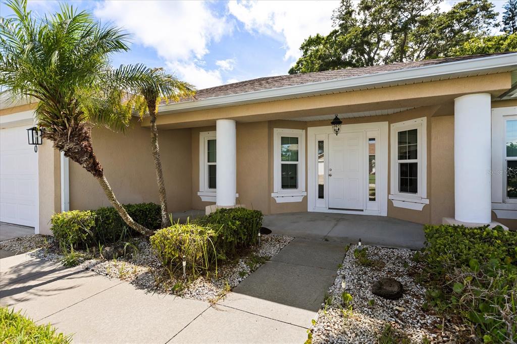 The exterior of a tan house features a covered entryway with white columns and landscaping — 410 CENTRAL MARINERS DRIVE, EDGEWATER, FL