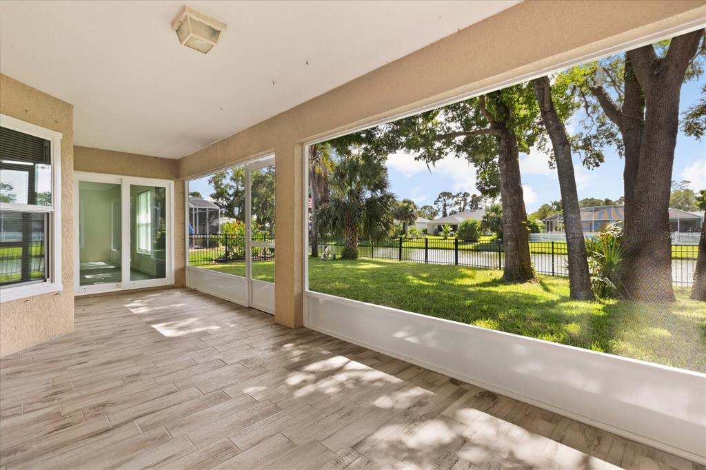 A screened-in patio with wood-look tile flooring overlooks a grassy yard, trees, and a pond — 410 CENTRAL MARINERS DRIVE, EDGEWATER, FL