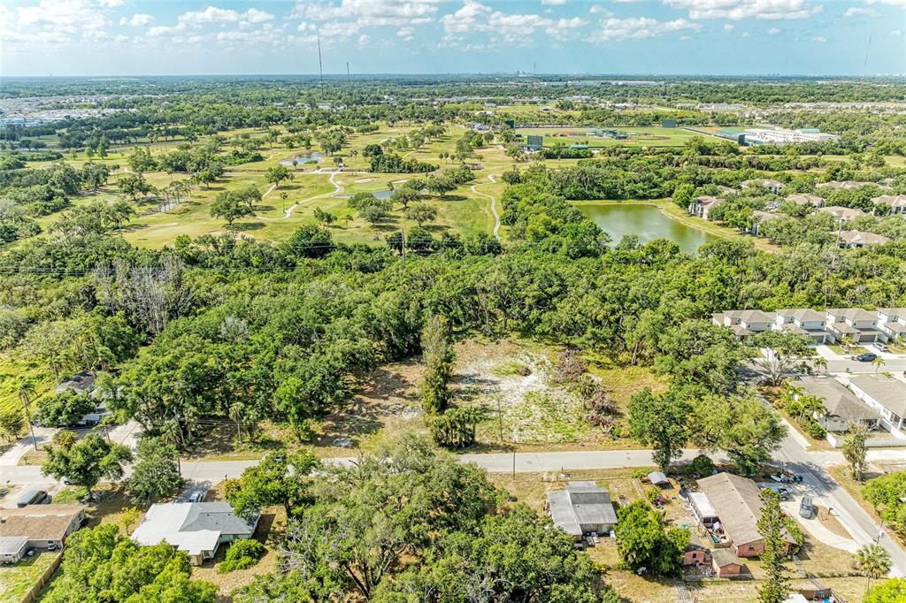An aerial view shows a vacant lot surrounded by trees, residential homes, and a golf course — 3006 12TH AVENUE E, BRADENTON, FL