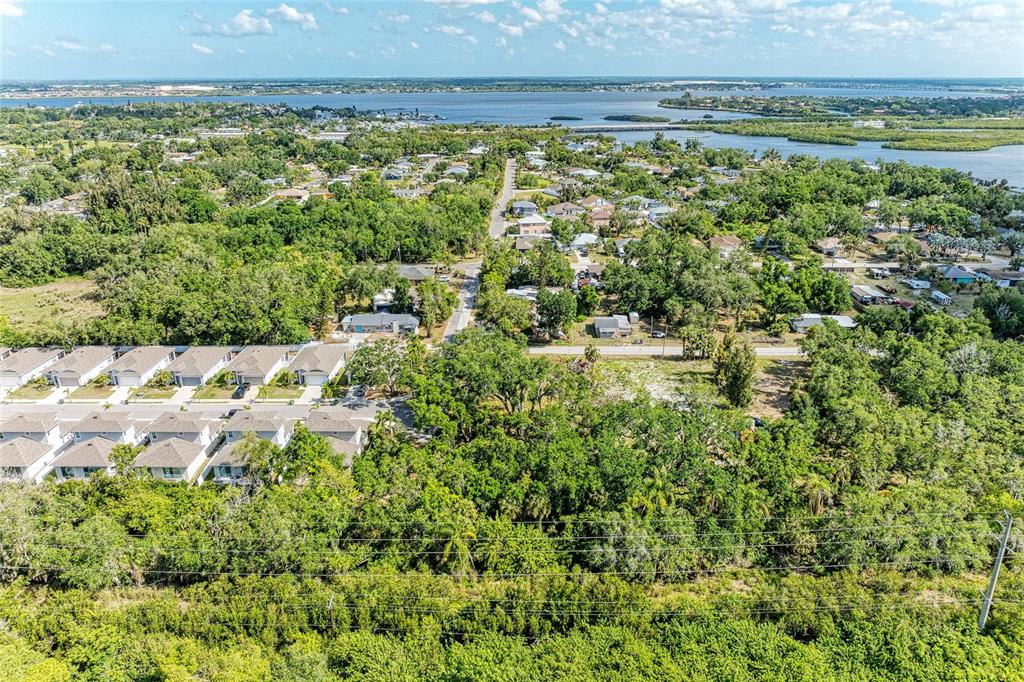 An aerial view shows a residential neighborhood with townhomes, wooded areas, and a distant bay — 3006 12TH AVENUE E, BRADENTON, FL