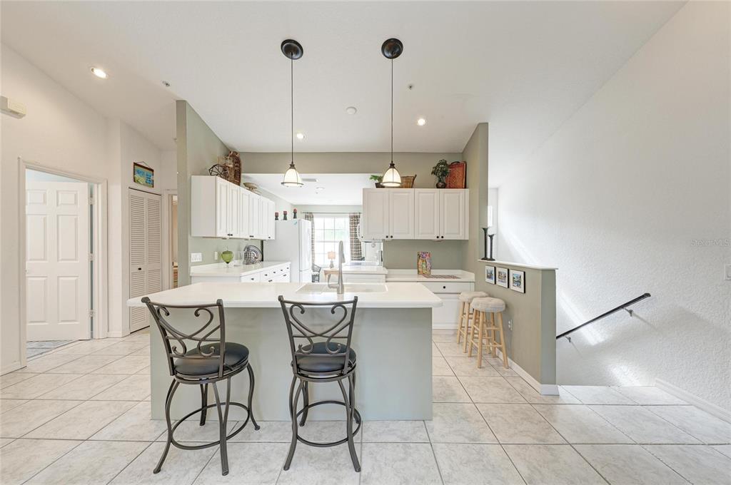 A kitchen features a central island with bar stools, white cabinetry, and light tile flooring — 6821 FAIRVIEW TERRACE UNIT 6821, BRADENTON, FL