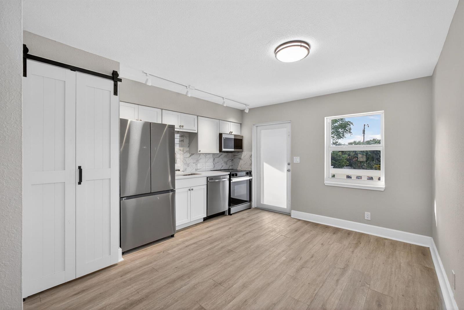 A kitchen with white cabinets, stainless steel appliances, and wood-look flooring next to a door — 624 Southwind Circle # 1, North Palm Beach FL 33408, NORTH PALM BEACH, FL