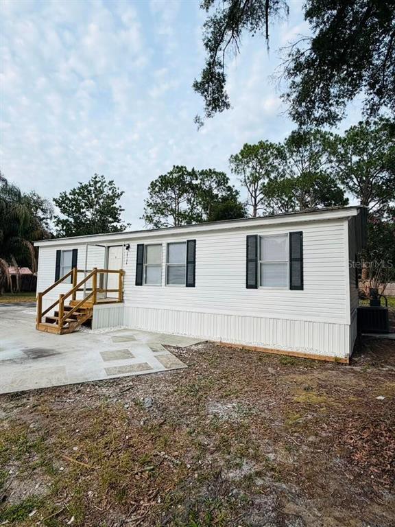 A white mobile home with black shutters and a wooden staircase sits on a concrete pad — 6734 RAVENWOOD STREET, ZEPHYRHILLS, FL