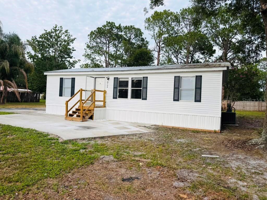 A white manufactured home with a wooden staircase leading to the front entrance — 6734 RAVENWOOD STREET, ZEPHYRHILLS, FL