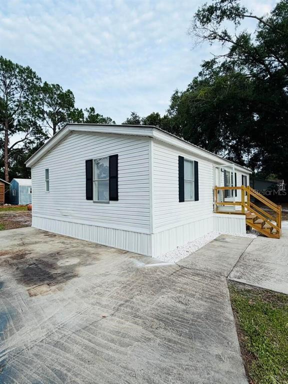 A white mobile home with black shutters and a wooden staircase sits on a concrete lot — 6734 RAVENWOOD STREET, ZEPHYRHILLS, FL