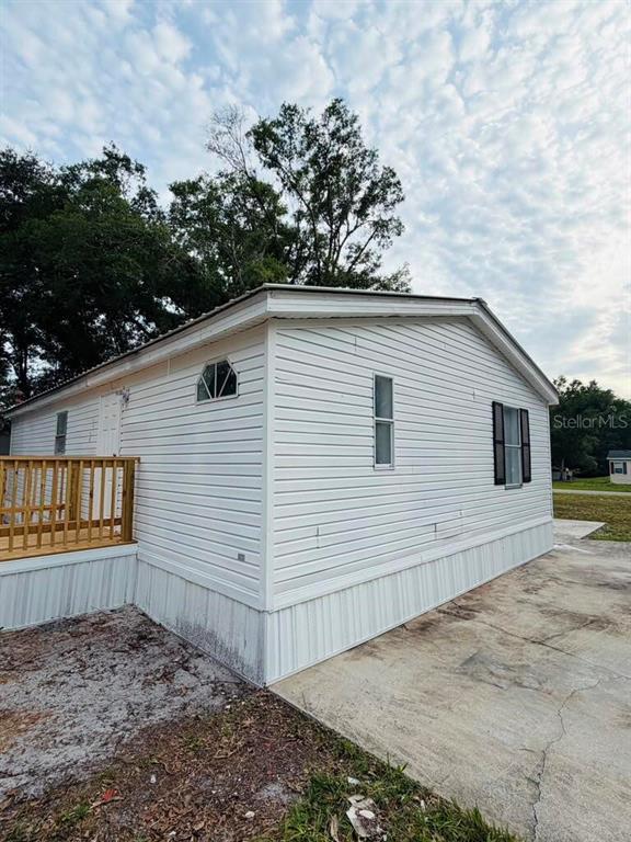 The exterior of a white mobile home features vinyl siding, a wooden deck, and windows — 6734 RAVENWOOD STREET, ZEPHYRHILLS, FL