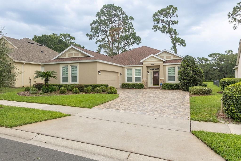 A single-story suburban house with a tan stucco exterior, paver driveway, and a front porch — 107 CURRY RISE COURT, DELAND, FL