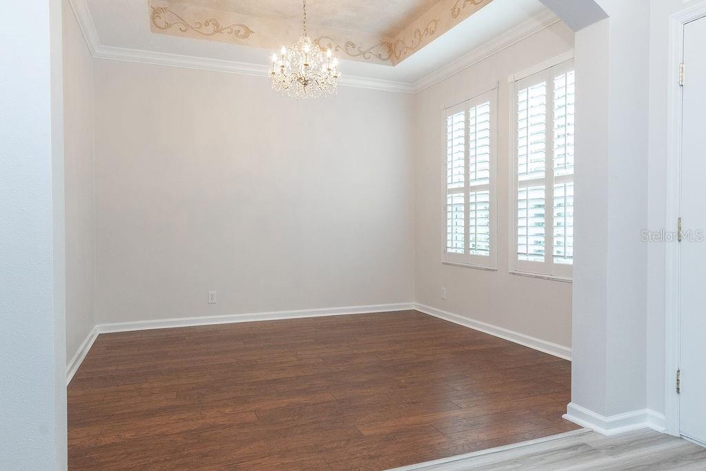 An empty dining room features wood-look flooring, a crystal chandelier, and a tray ceiling — 107 CURRY RISE COURT, DELAND, FL