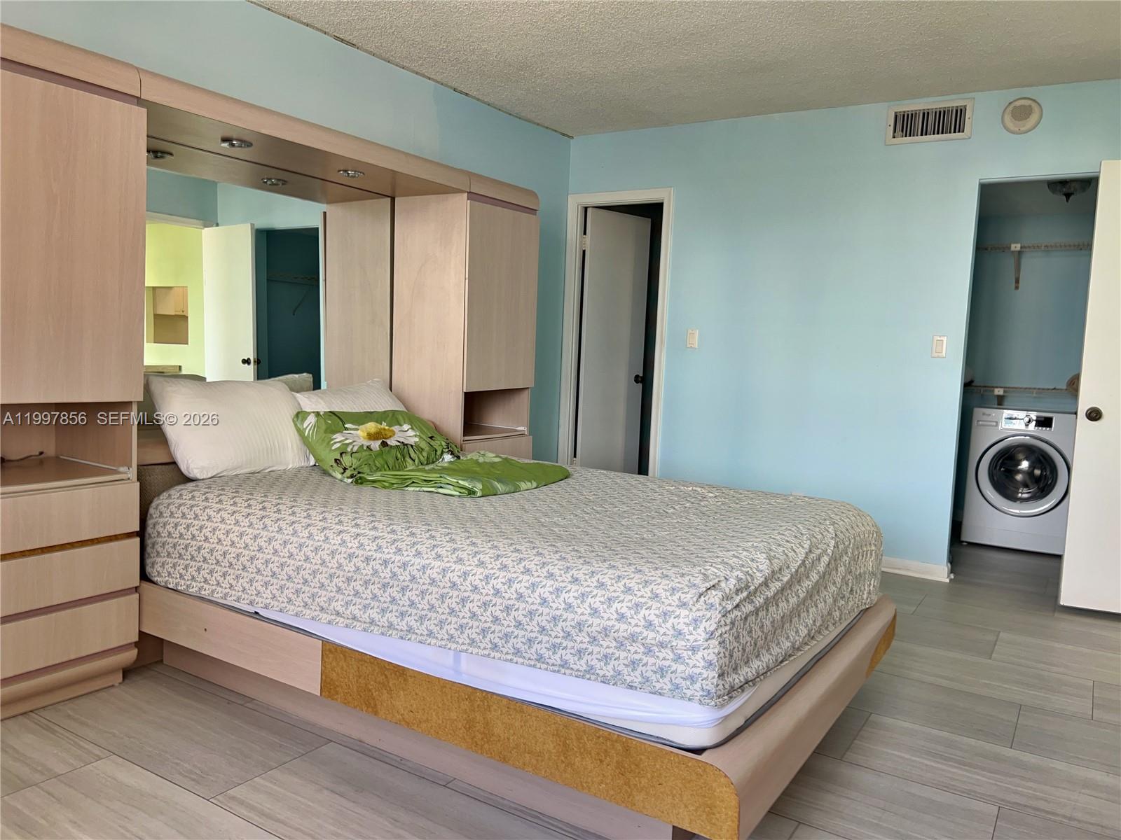 A bedroom features a light wood headboard unit, light blue walls, and an in-room washer — 1801 S Ocean Dr # 934, Hallandale Beach FL 33009, HALLANDALE BEACH, FL