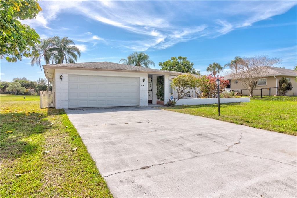 A single-story house with a white garage door and a concrete driveway under a blue sky — 37 OAKLAND HILLS PLACE, ROTONDA WEST, FL