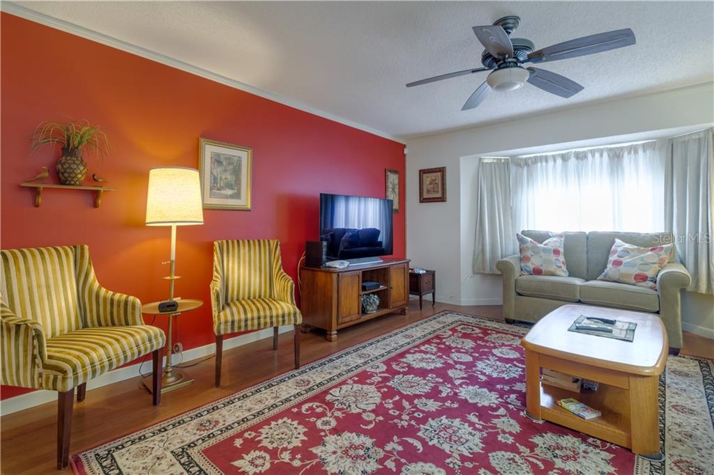 A living room features a red accent wall, striped chairs, a sofa, and a patterned rug — 37 OAKLAND HILLS PLACE, ROTONDA WEST, FL