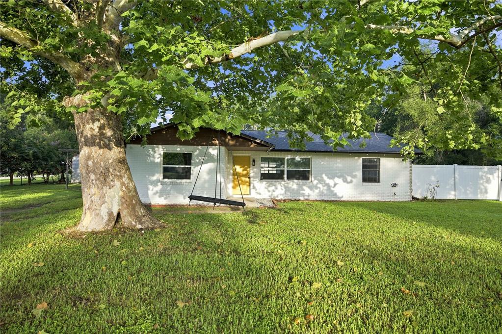 A white brick house with a yellow front door sits behind a large shade tree — 13720 SE 36TH AVENUE, SUMMERFIELD, FL
