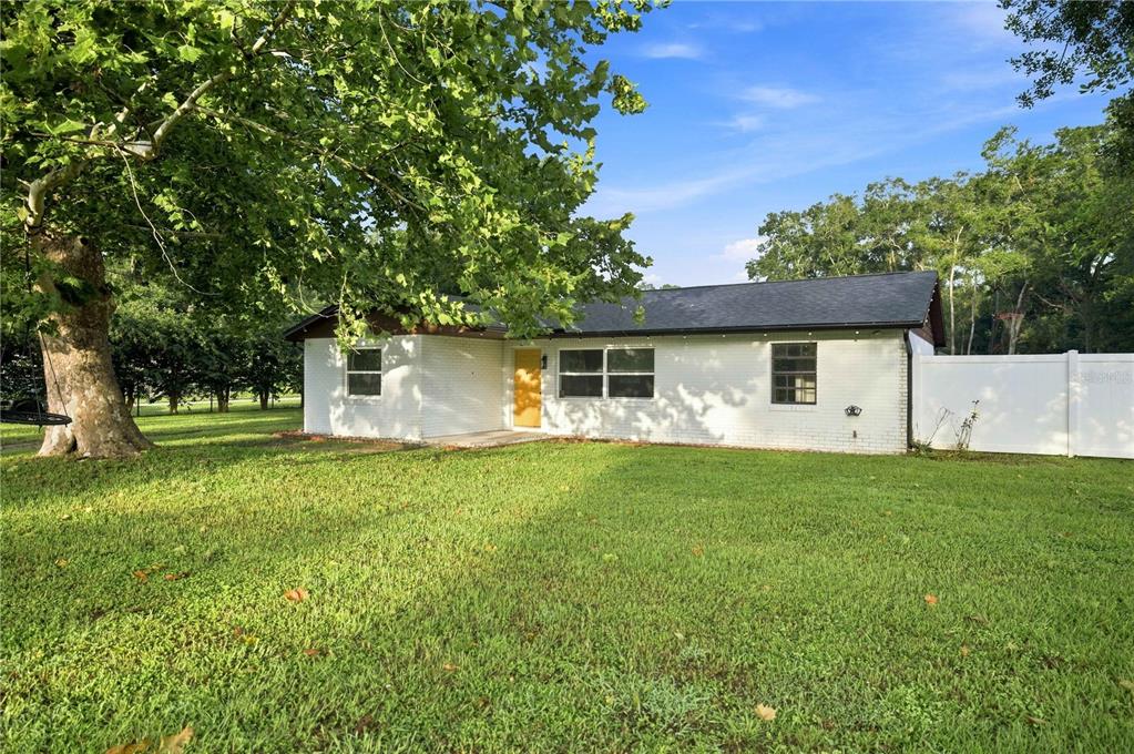 A single-story white brick house with a yellow front door sits on a grassy lot — 13720 SE 36TH AVENUE, SUMMERFIELD, FL