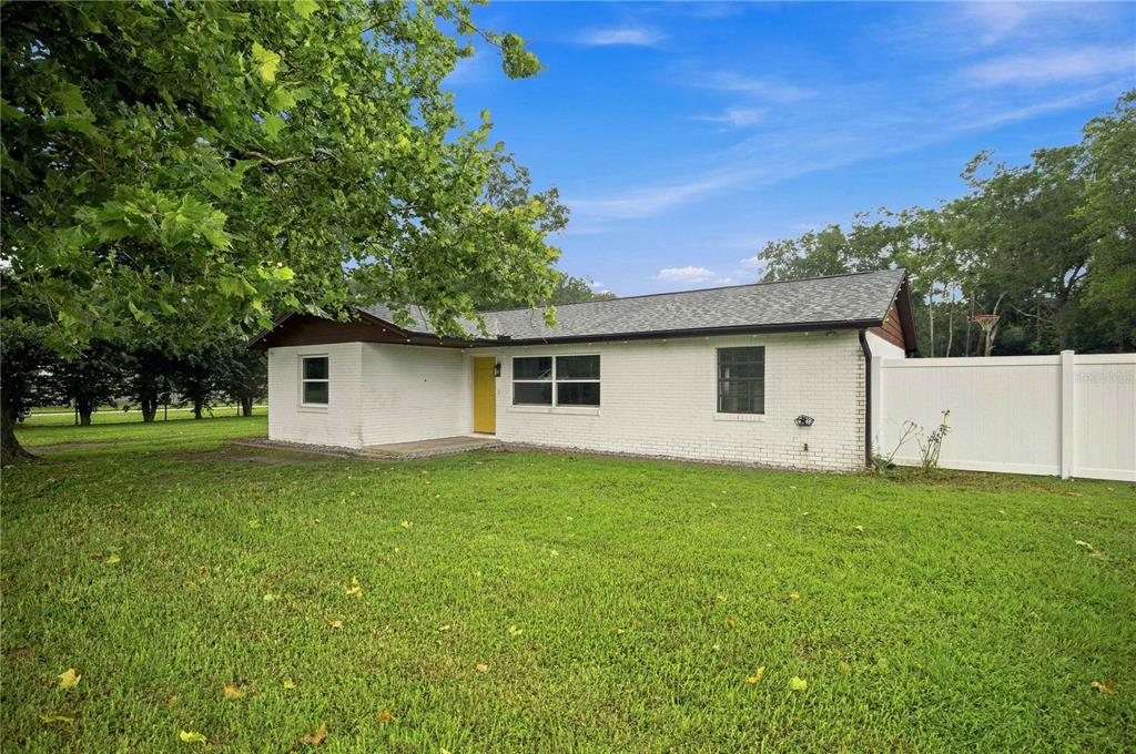 A single-story white brick house with a yellow front door and a white vinyl fence — 13720 SE 36TH AVENUE, SUMMERFIELD, FL