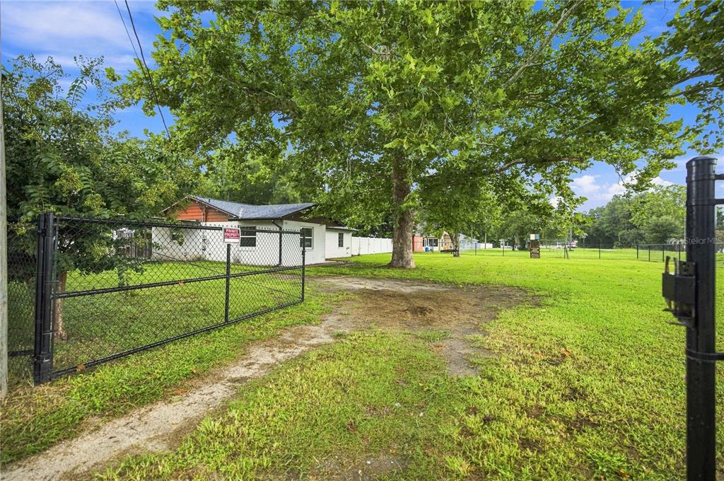 A gated gravel driveway leads to a small house shaded by a large tree — 13720 SE 36TH AVENUE, SUMMERFIELD, FL