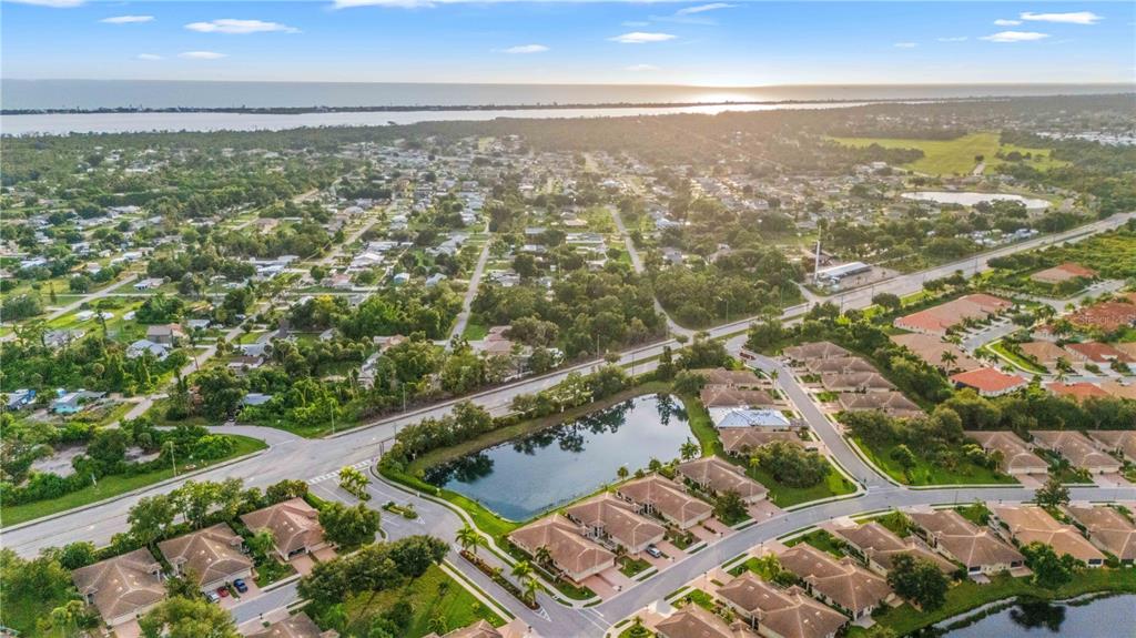 An aerial view shows a suburban neighborhood with houses, a pond, and a nearby road — 1001 TOPELIS DRIVE, ENGLEWOOD, FL
