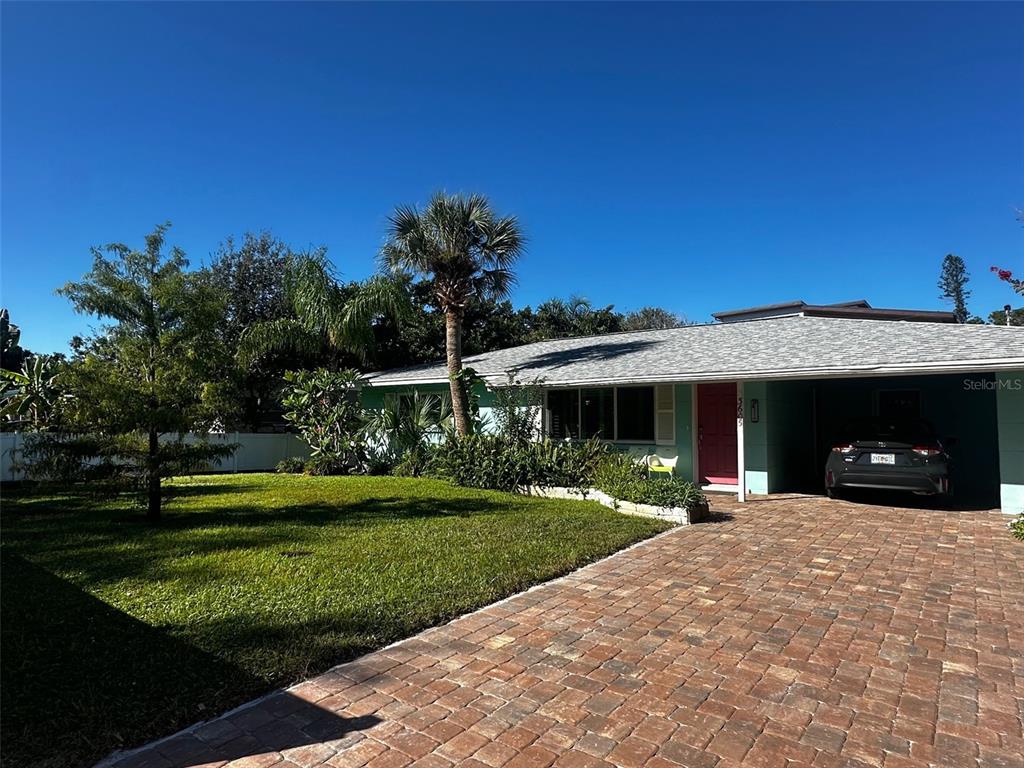 A single-story house with a brick driveway, palm tree, and green exterior sits under blue skies — 3605 IROQUOIS AVENUE, SARASOTA, FL