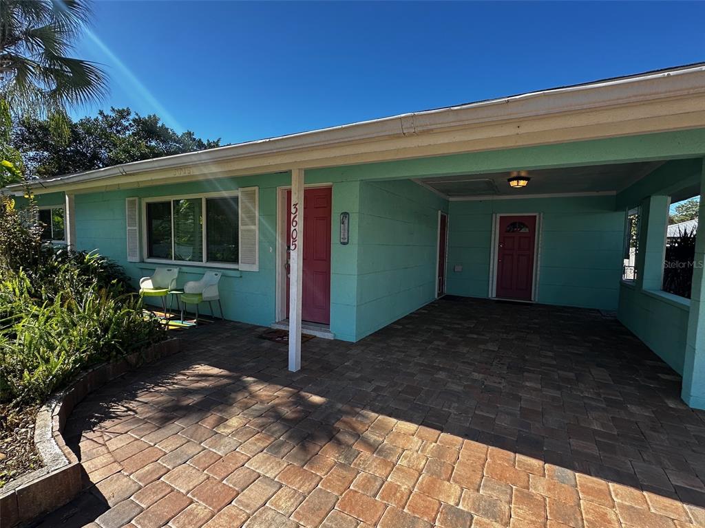 A teal house exterior features a brick-paved patio, a carport, and two red front doors — 3605 IROQUOIS AVENUE, SARASOTA, FL
