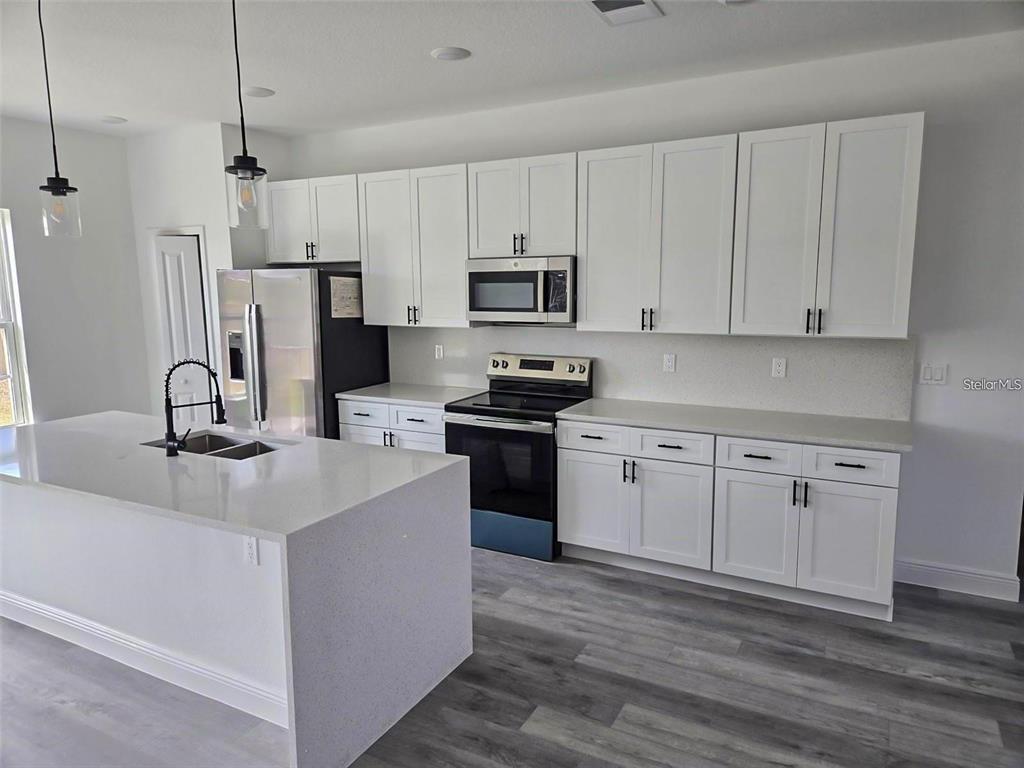 A modern kitchen features white cabinets, quartz countertops, stainless steel appliances, and a central island — 15092 SW 52ND COURT, OCALA, FL