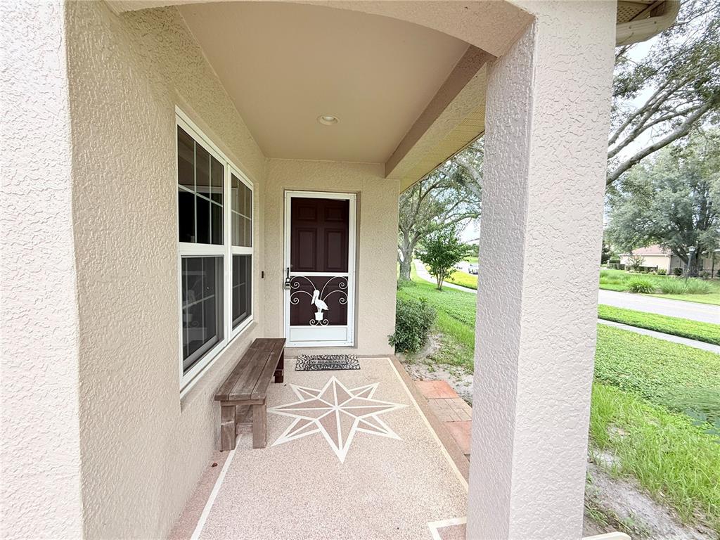 A covered front porch features a decorative star inlay on the floor and a bench — 265 CENTER OAK CIRCLE, SPRING HILL, FL