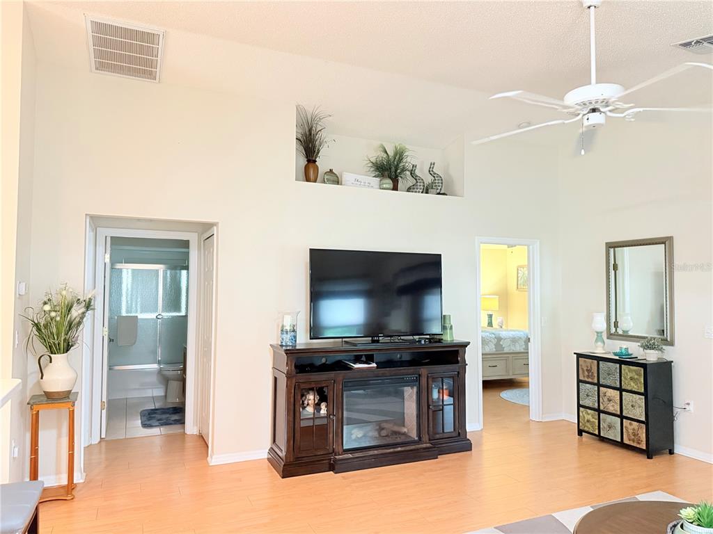 A living room features a television on a media console, light wood flooring, and high ceilings — 265 CENTER OAK CIRCLE, SPRING HILL, FL