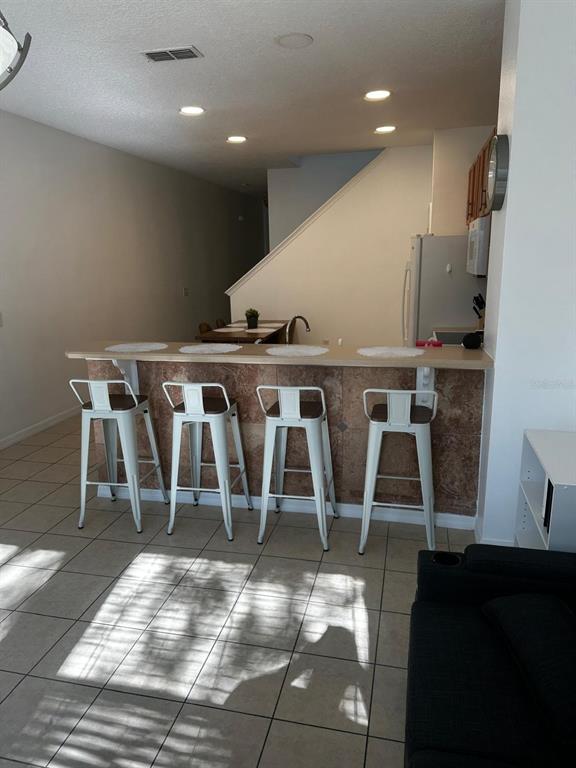 A kitchen features a tiled breakfast bar with four white metal stools on a tiled floor — 5104 DOMINICA DRIVE, KISSIMMEE, FL