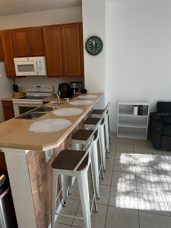 A kitchen features wooden cabinets, a breakfast bar with four stools, and tiled flooring — 5104 DOMINICA DRIVE, KISSIMMEE, FL