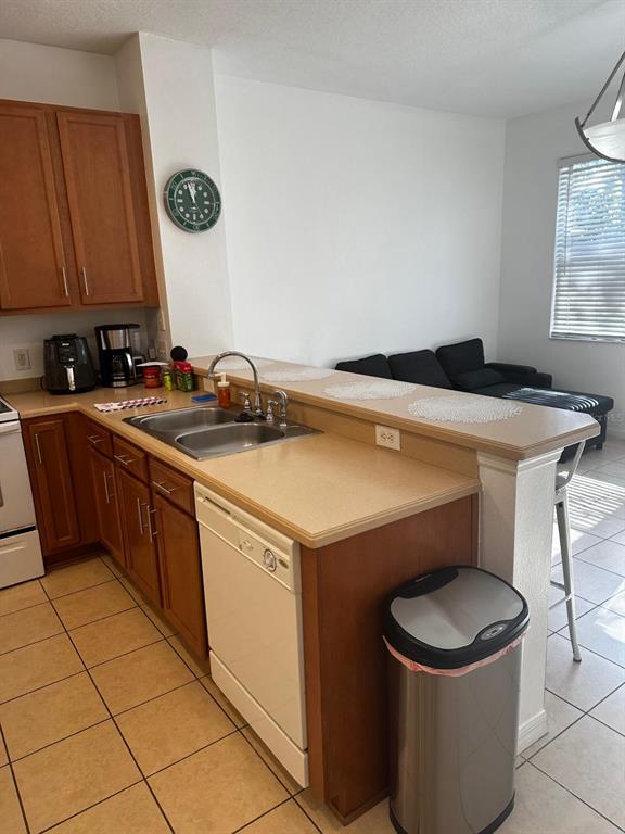A kitchen with wood cabinets, tan countertops, and a dishwasher overlooks a living area — 5104 DOMINICA DRIVE, KISSIMMEE, FL