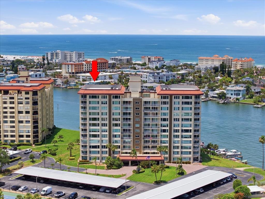 An aerial view shows a multi-story residential building situated on a waterfront with parking — 736 ISLAND WAY UNIT 1003, CLEARWATER BEACH, FL