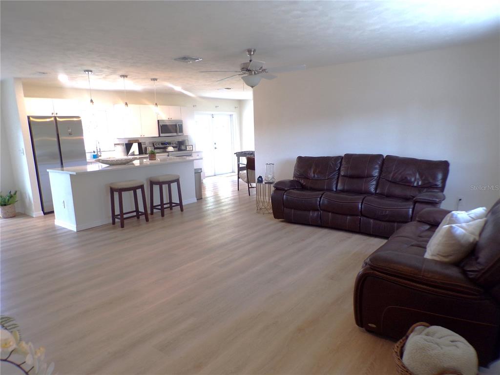 An open-concept living room and kitchen featuring light wood flooring and dark leather sofas — 1148 SALINA AVENUE, PORT CHARLOTTE, FL