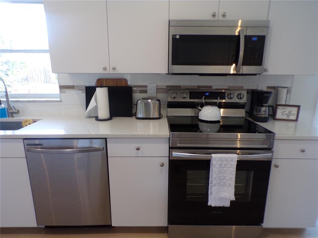A kitchen features white cabinets, stainless steel appliances, a white countertop, and a tiled backsplash — 1148 SALINA AVENUE, PORT CHARLOTTE, FL
