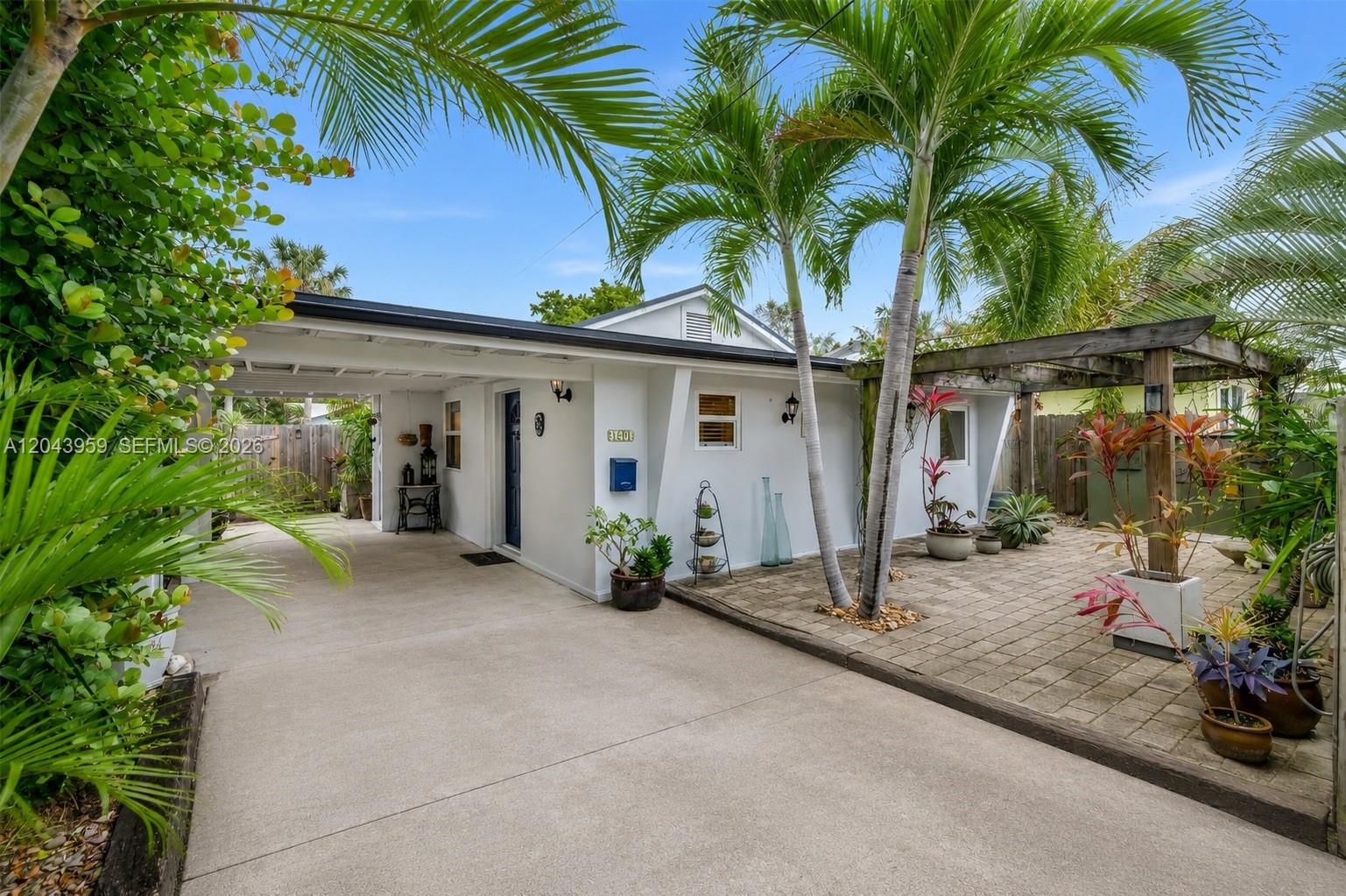 A white house features a concrete driveway, a carport, and a paved patio with palm trees — 1401 NE 33rd St, Oakland Park FL 33334, OAKLAND PARK, FL